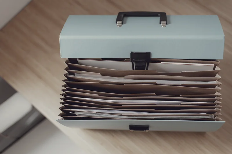 An open accordion file on a wooden desk, with the papers sorted into its dividers.