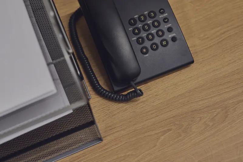 A desk with a landline phone and a document tray on a wooden top.