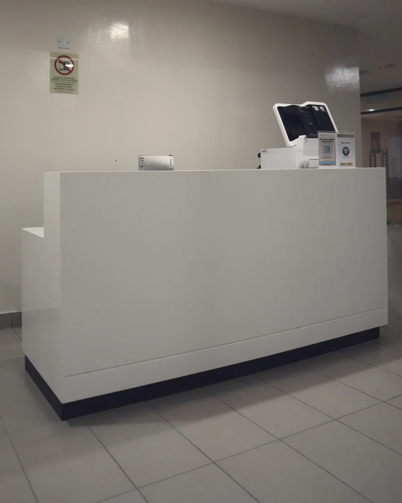 Empty clinic front desk: a white counter with a monitor on a tiled floor.